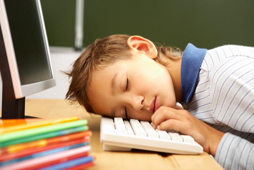 Portrait of cute lad sleeping with his head on computer keyboard in classroom